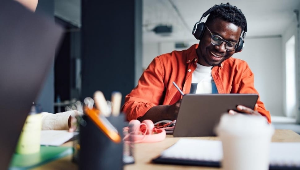 Young man with glasses and headphones works on a laptop computer.