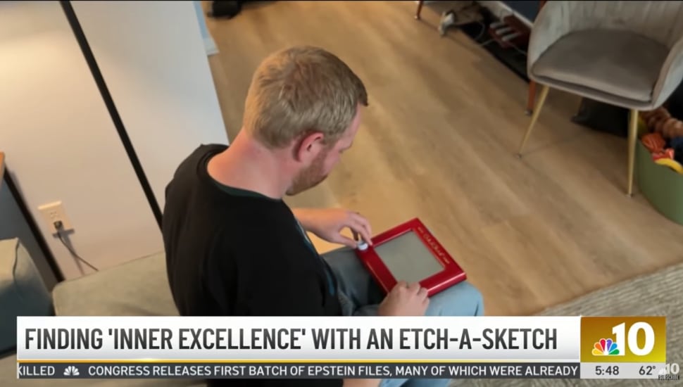 John Obringer sitting on his couch, using an Etch A Sketch on his lap.