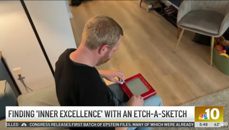 John Obringer sitting on his couch, using an Etch A Sketch on his lap.