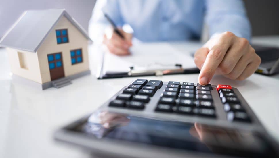 Close-up Of A Hand Calculating A Real Estate Property Tax On Desk.
