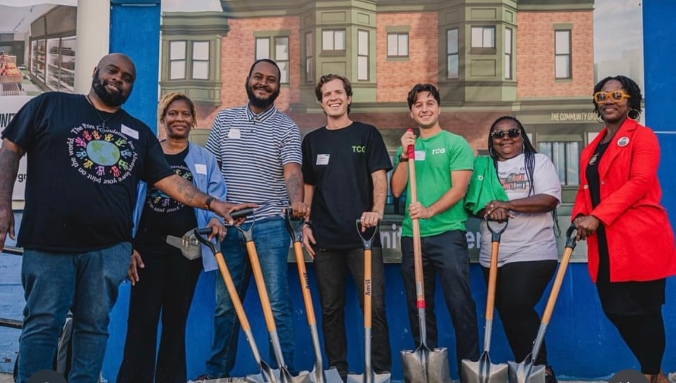 Seven people holding a shovel to signify a groundbreaking.