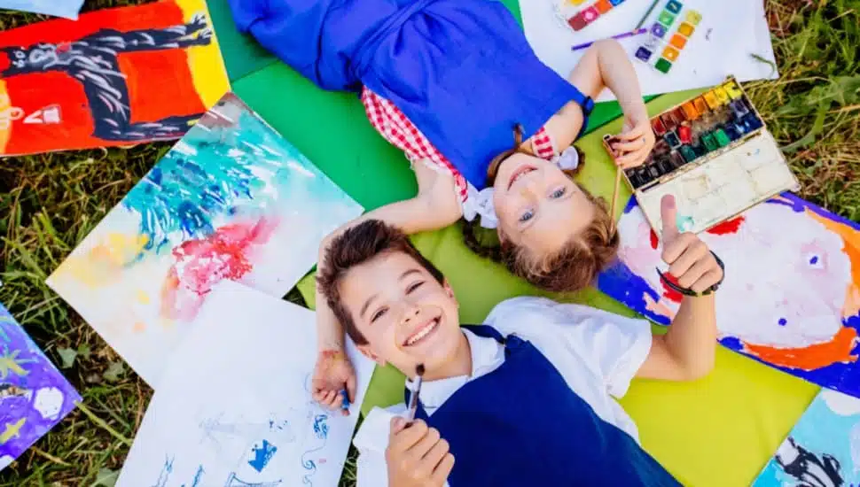 Children lie on the grass with their drawings next to them. kids on the ground with drawings.