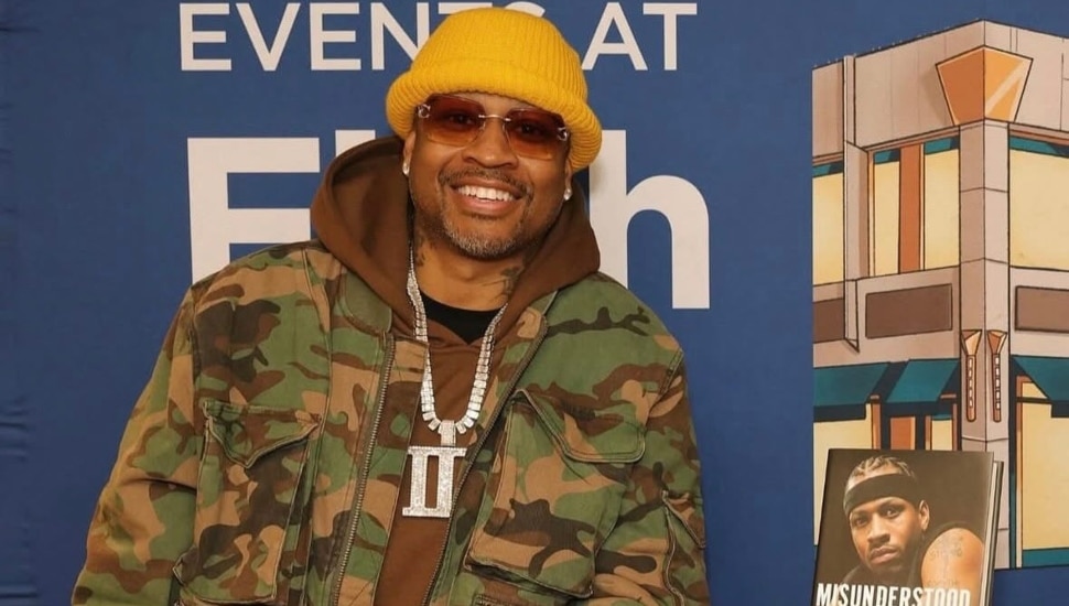Allen Iverson smiling and posing next to a copy of his new memoir, "Misunderstood."