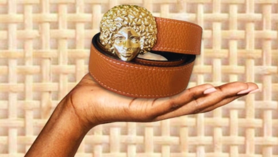 A hand holding a belt with a woman's face as the belt buckle.