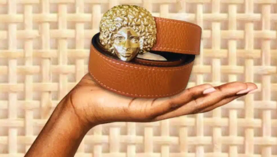 A hand holding a belt with a woman's face as the belt buckle.