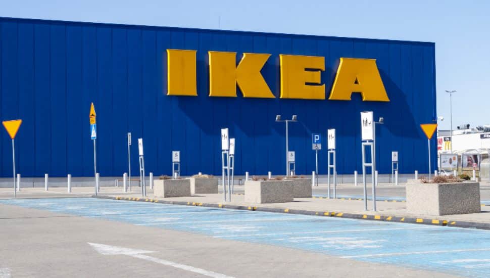 The front of an IKEA a blue IKEA store with a yellow IKEA sign along with a delivery and pick up zone in the parking lot.