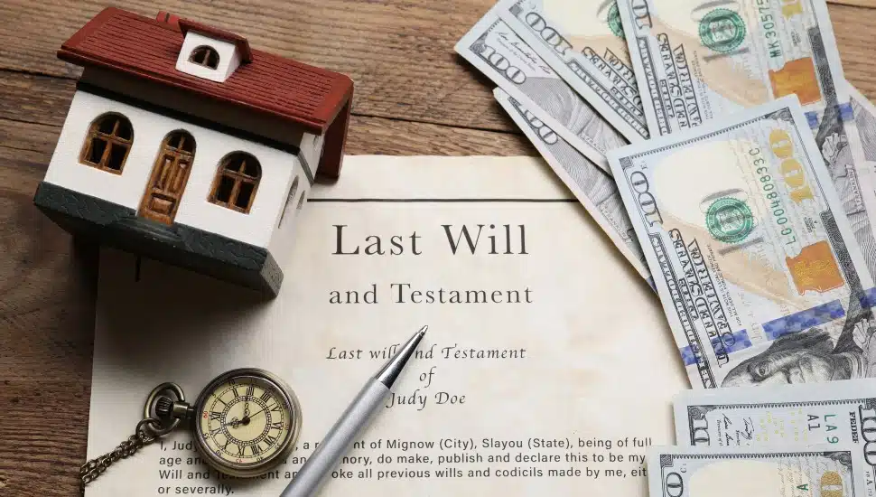 Last Will and Testament, pocket watch, dollar bills, house model and pen on a wooden table.