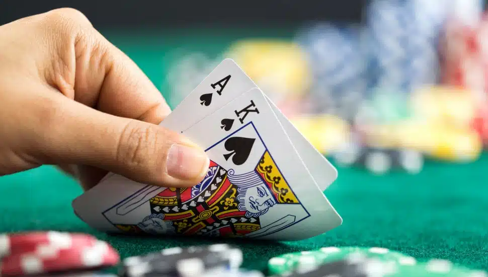 Gambling hand holding an "King" and "Ace" poker cards and money chips on the table.