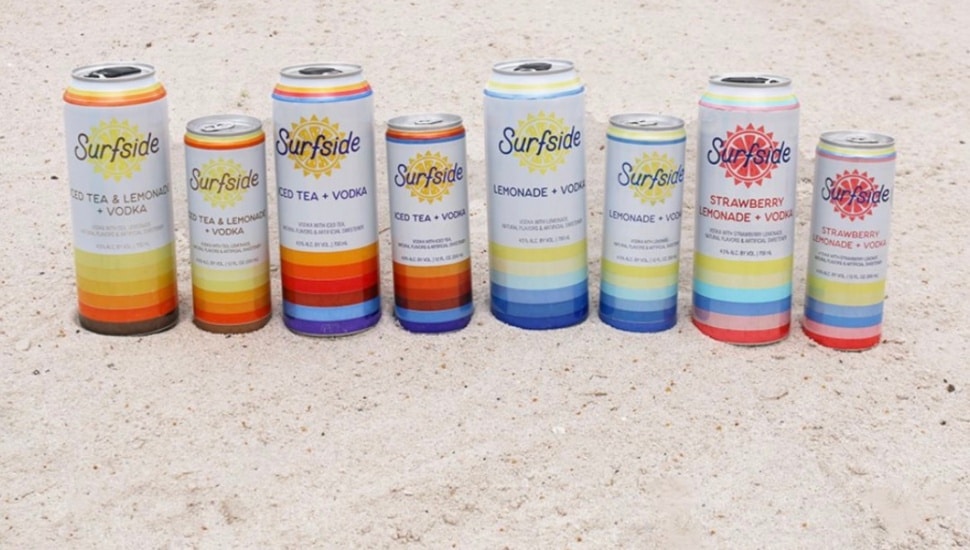 Eight cans of Surfside drinks next to each other on the beach.