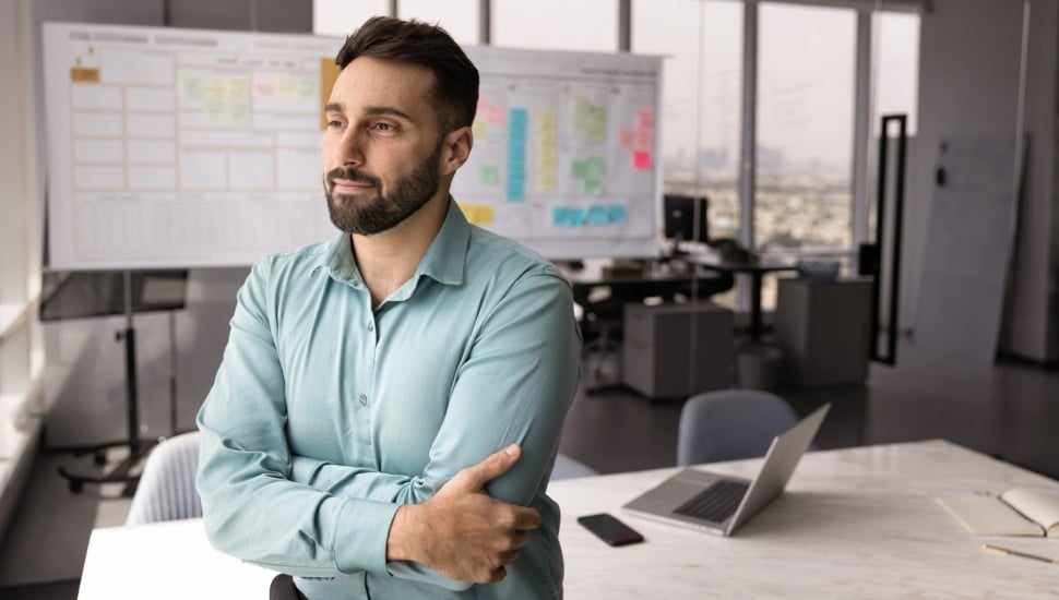Thoughtful professional man stands with arms crossed in modern office.