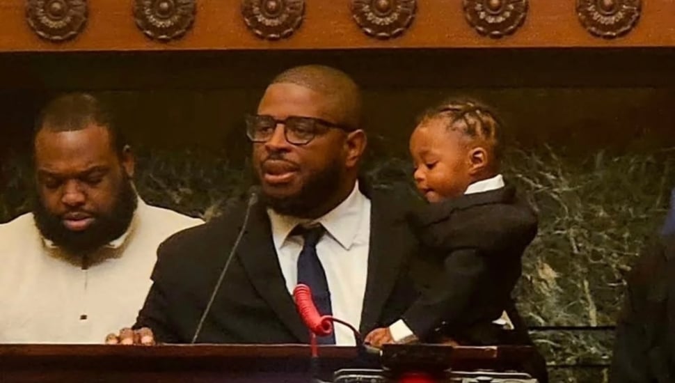 Anton Moore at a podium holding his young son.