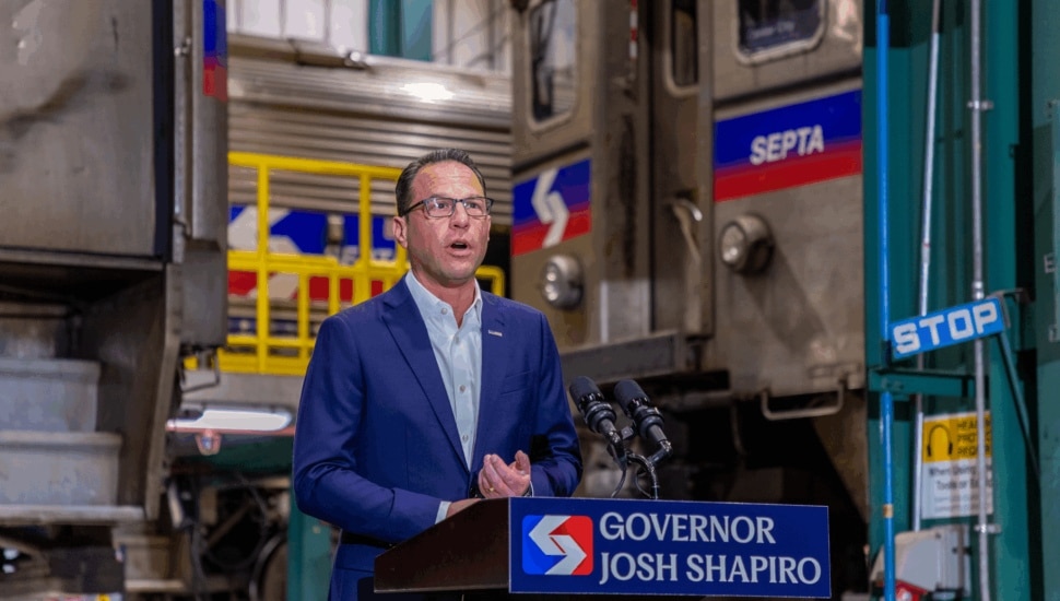 Gov. Josh Shapiro speaking at a podium with a SEPTA car behind him.