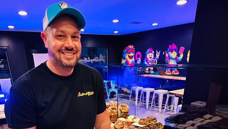 Robert Weinrich inside PanDoughMonium Bakery with treats behind him.