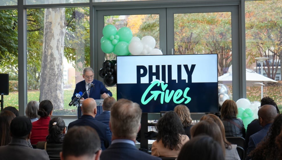 Pedro Ramos speaking at a podium in front of a crowd with a monitor that reads "Philly Gives" in the background.