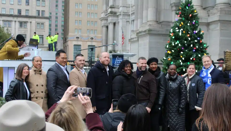 City officials and partners of this year's holiday tree arrival and lighting celebration with tree in the background.