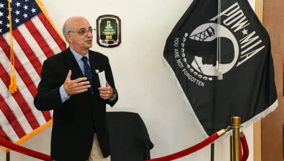 Ralph Galati speaking with an American flag and POW/MIA flag in the background.
