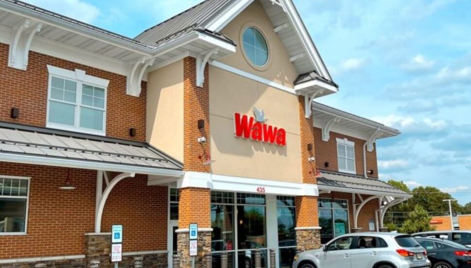 The front of a Wawa store with the Wawa sign visible and parked cars.