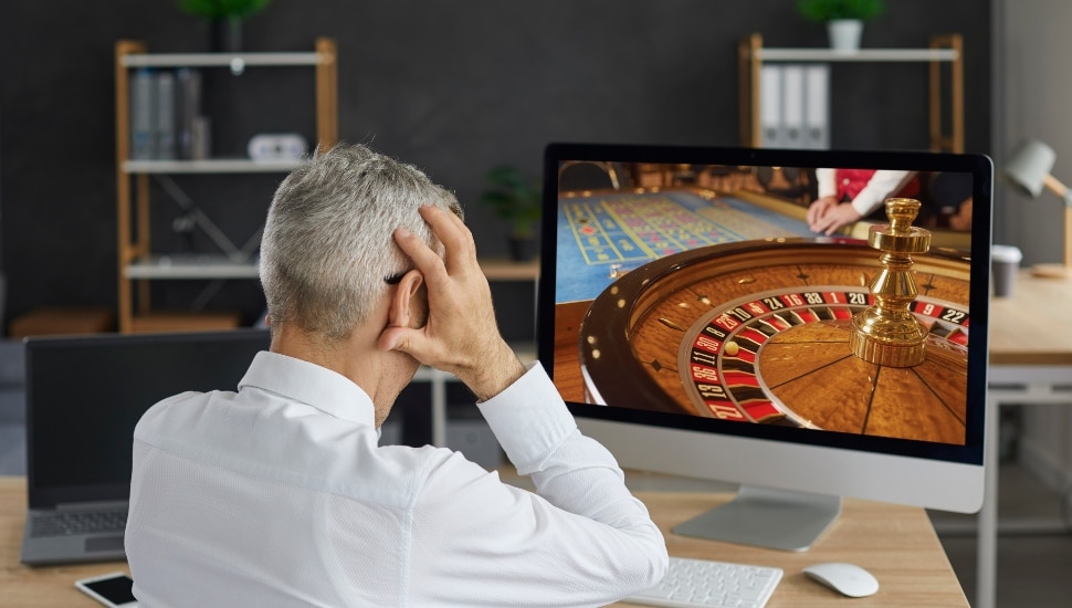 Man online gambling with hands over face after likely loss.