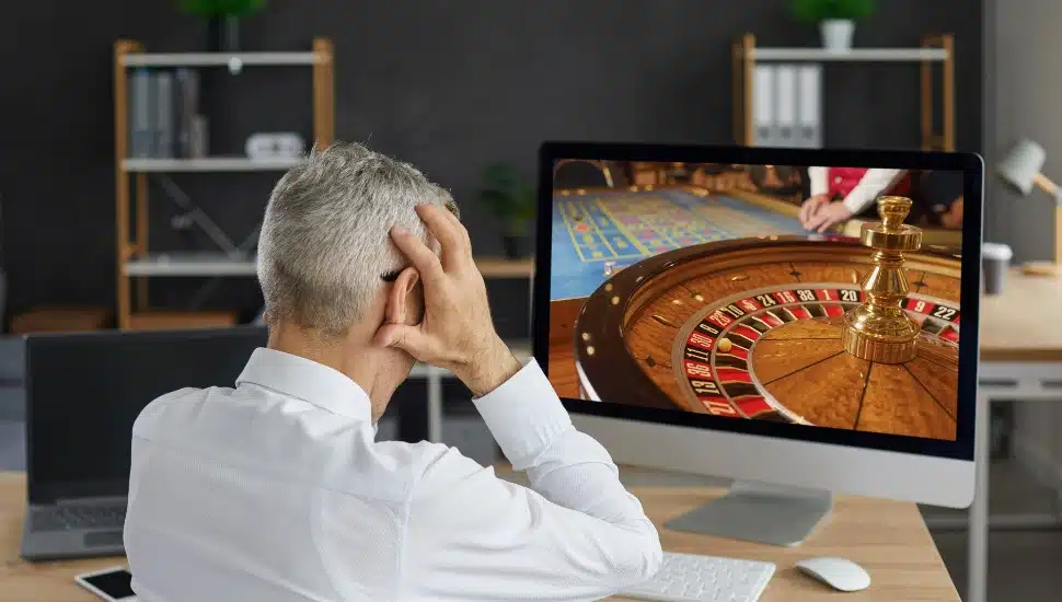 Man online gambling with hands over face after likely loss.