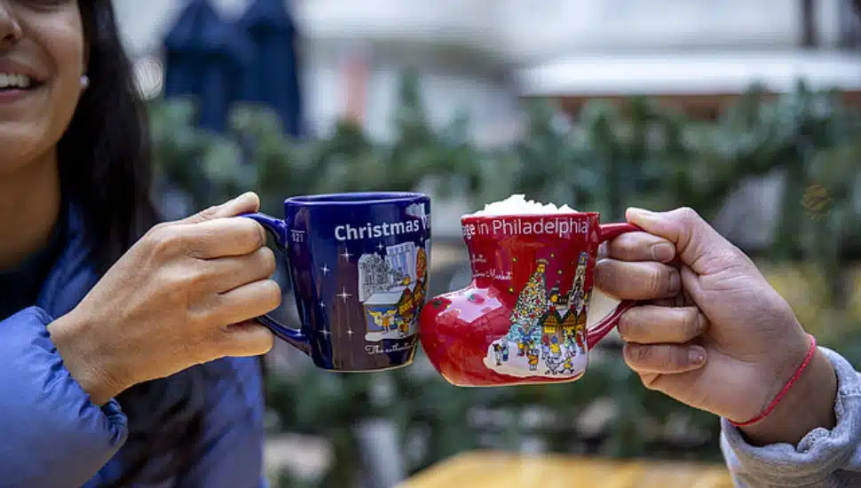 Two hands holding mugs of hot beverages at Christmas Village.