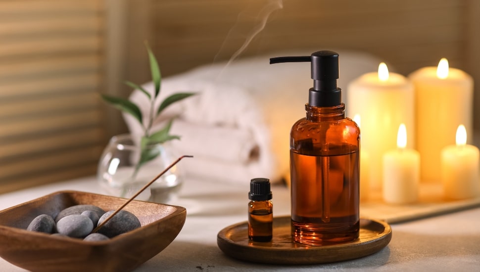 Candles, stones, essential oils and towels on and near a white wooden table.