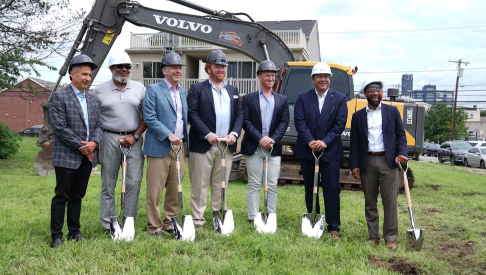 Men in business attire hold shovels at groundbreaking ceremony.