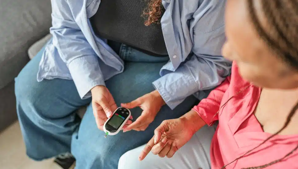 A Black woman making blood glycemia test to her mother for diabetes check at home.
