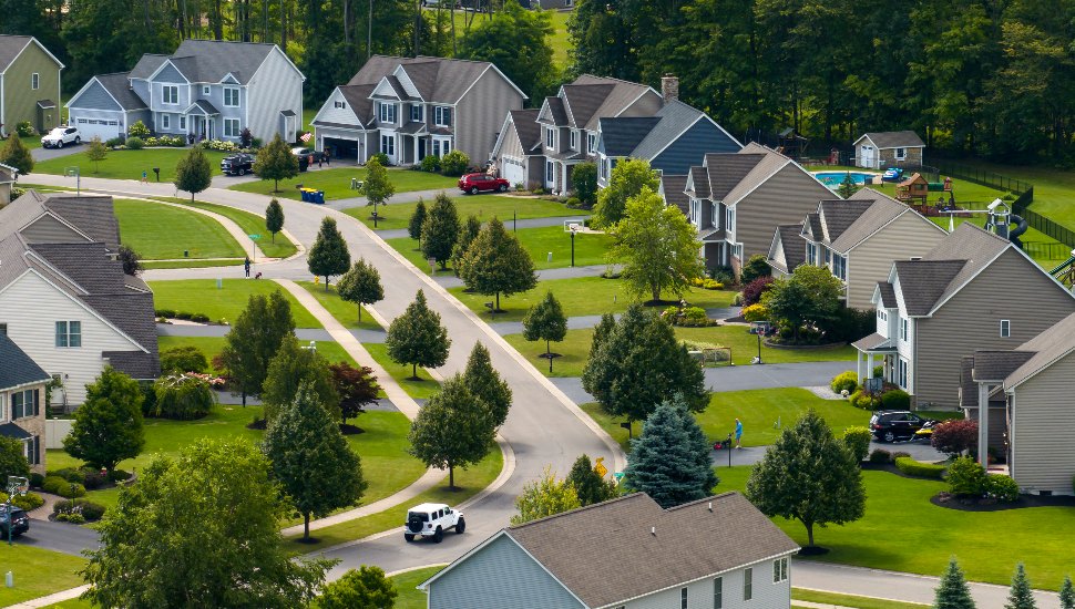 Suburban neighborhood aerial view with lots of homes and a road.