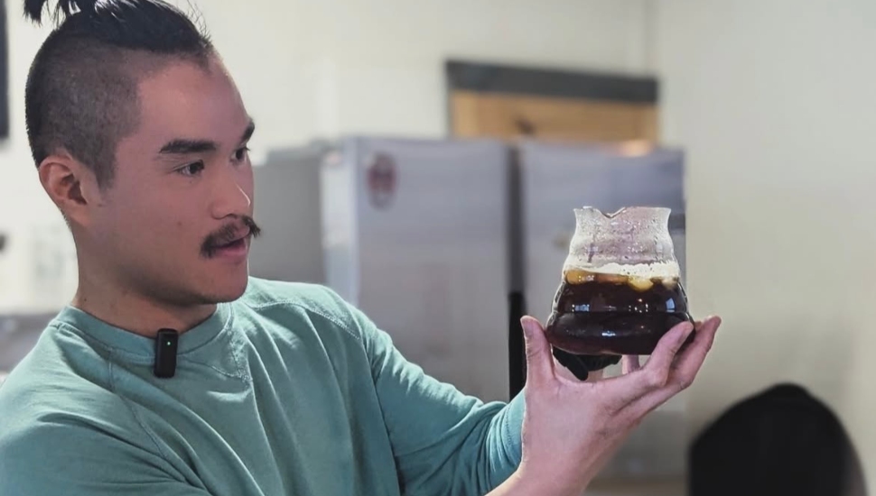 Joseph Nguyen holding a glass mug of coffee.