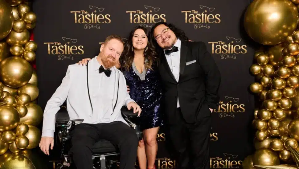 Eli Kulp, Marisa Magnatta and Dave Wez with "The Tasties" backdrop behind them with gold balloons.