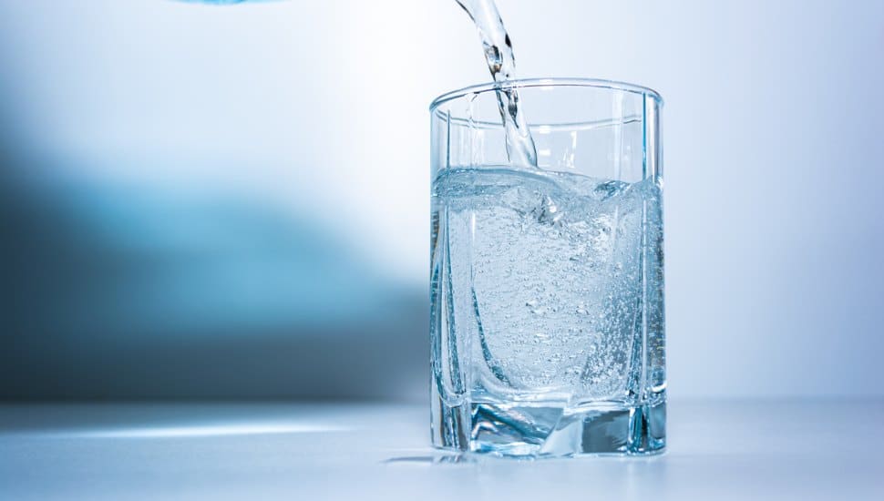 Pouring mineral water into a glass beaker. The photo shows part of a plastic bottle and an almost full glass of water with gas bubbles.