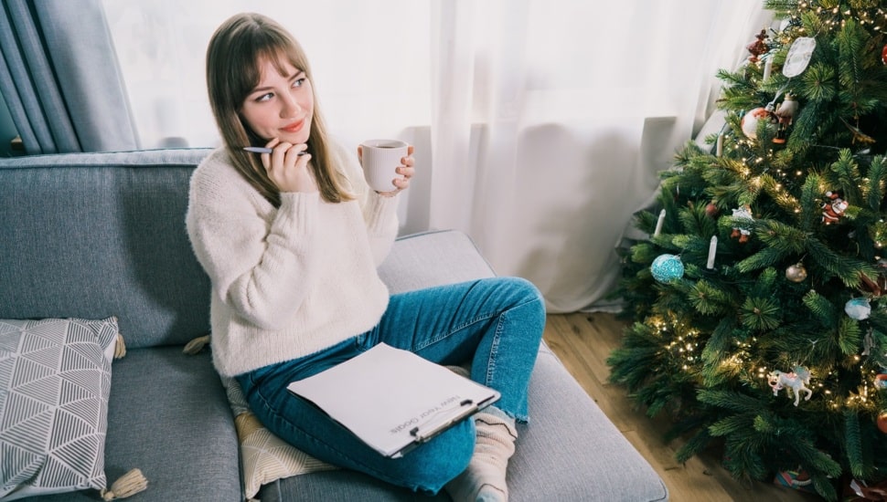 Young woman with coffee mug is writing new year's goals on clipboard.