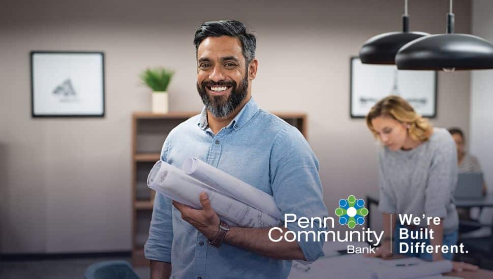 Small business owner holding blueprints in a collaborative workspace supported by Penn Community Bank.