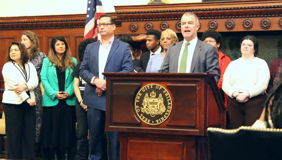 Adam Thiel speaking at a podium with Orlando Rendon to his right, surrounded by several others.