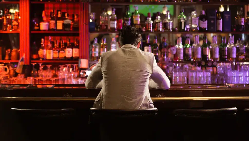 Back view of a young man drinking beer while while sitting at the bar counter.
