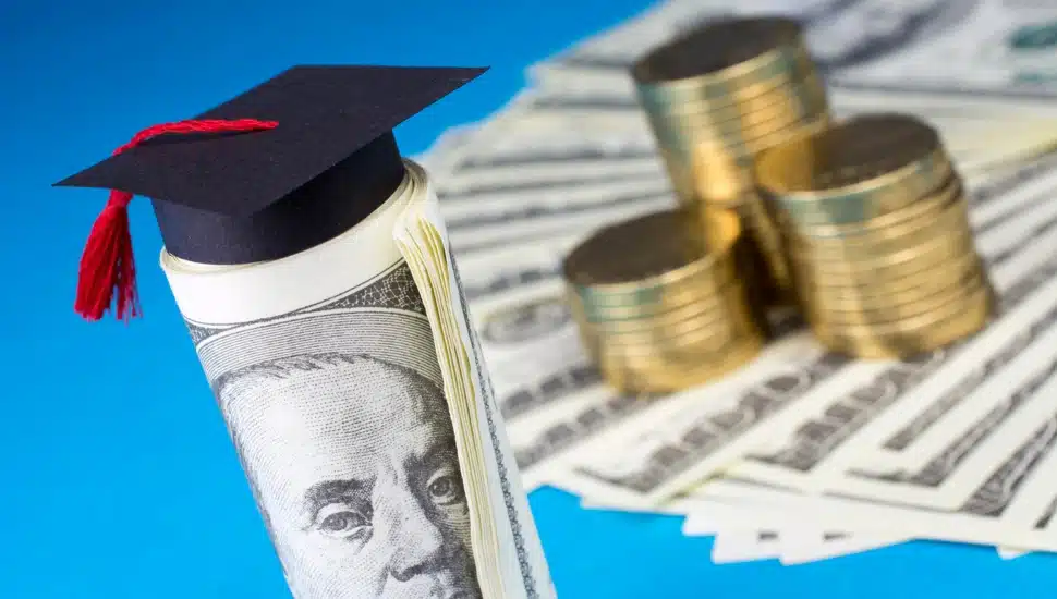 Graduation mortarboard, money, and gold coins on blue background.