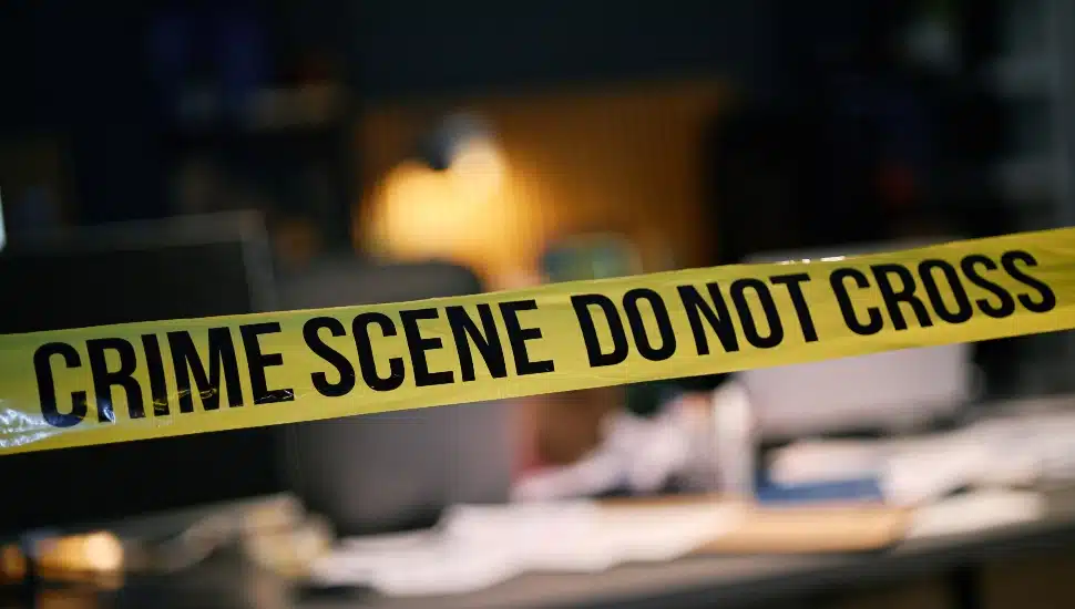 Yellow crime scene tape cordoning off an area inside building with various blurred objects in background.