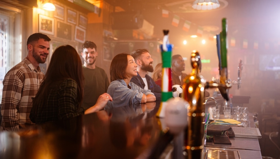 Diverse group of happy friends gathered at a bar, watching a sports game and enjoying an evening of socializing.