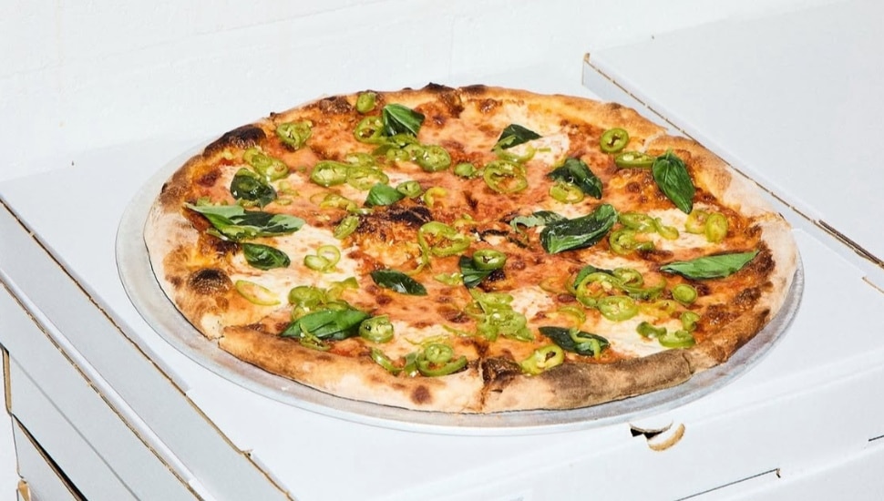 A pizza pie on top of a stack of pizza boxes.