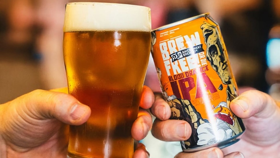 Two hands: One with a glass of beer and another with a can of beer, toasting one another.