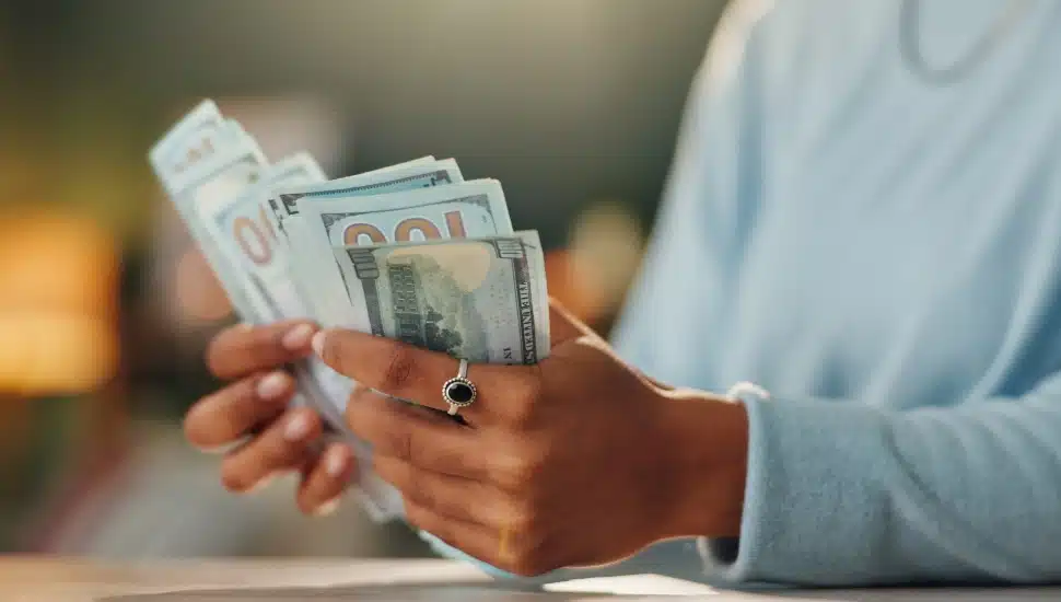 A hand counting money, mostly hundred dollar bills.