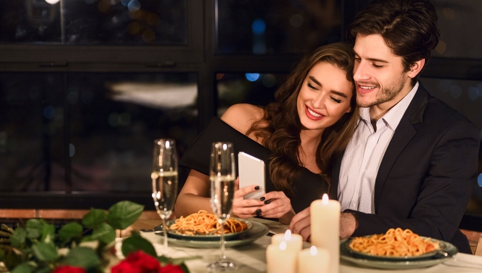 Happy couple looking photos on smartphone during romantic dating in restaurant.