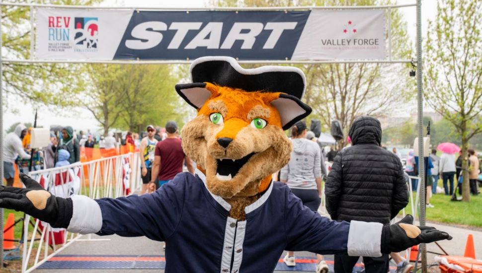 The Valley Forge Tourism & Convention Board mascot, Monty the Fox stands in front of the starting line at the Rev Run in Valley Forge.