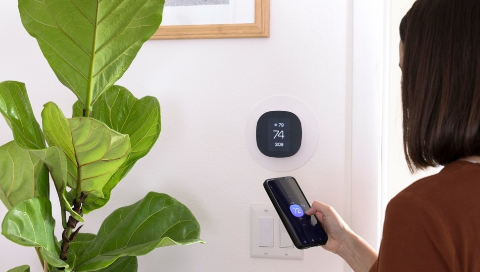 Woman adjusts room temperature on thermostat.