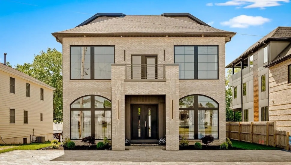 Exterior of a custom-built luxury home at 9741 Krewstown Road in Philadelphia featuring light brick facade, arched windows, black double entry doors, and a second-floor balcony.