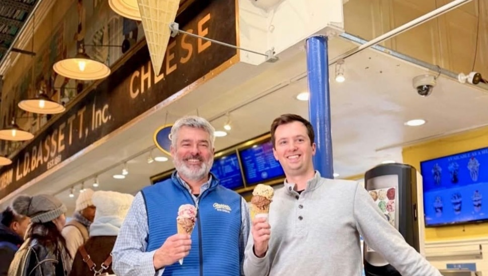 Two men smile and hold ice cream cones in front of the L.D. Bassett, Inc. storefront inside Reading Terminal Market in Philadelphia.