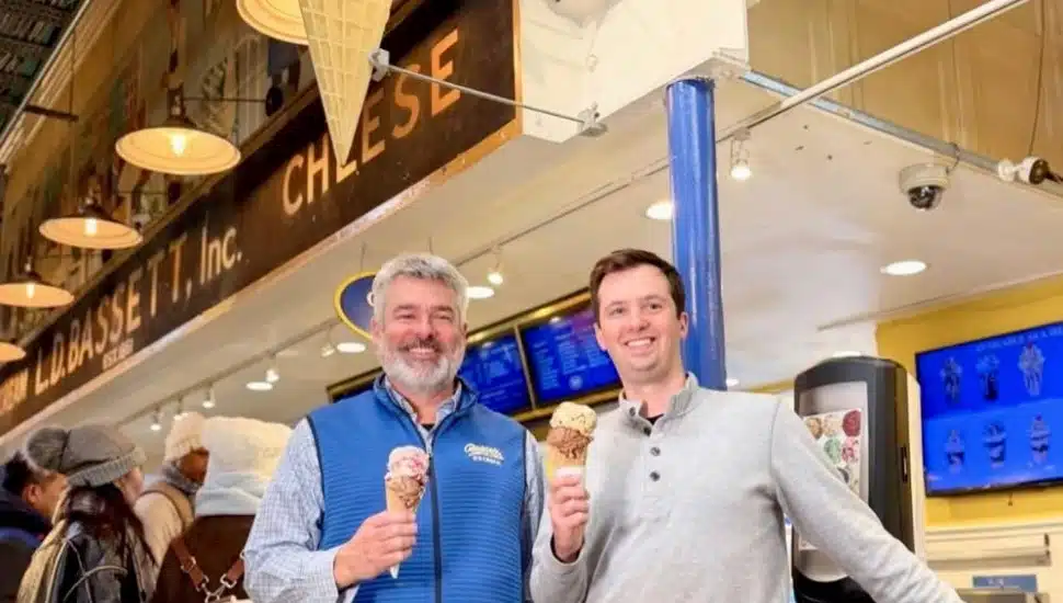 Two men smile and hold ice cream cones in front of the L.D. Bassett, Inc. storefront inside Reading Terminal Market in Philadelphia.