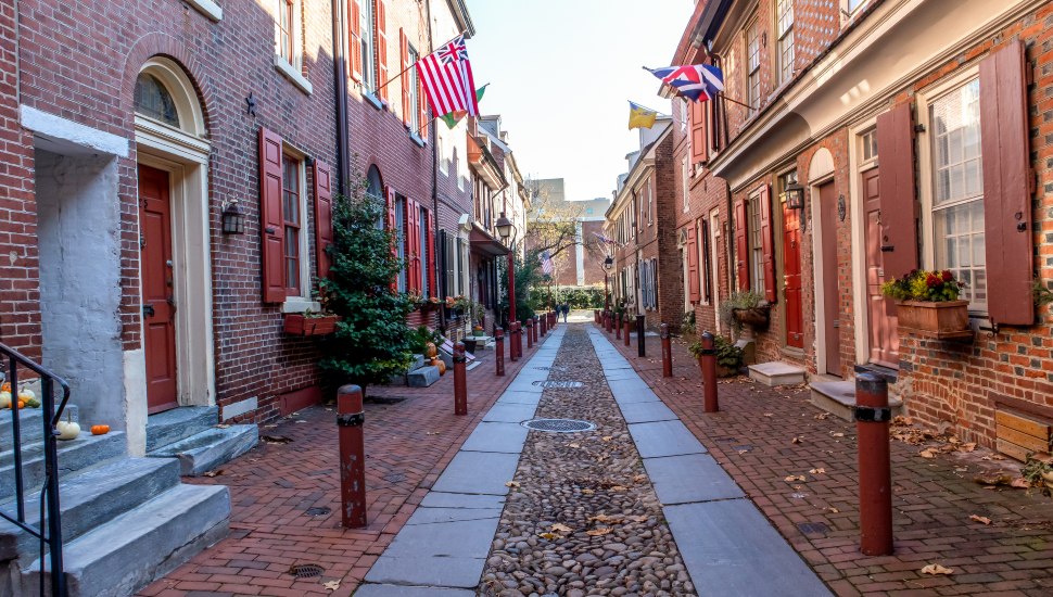 Elfreth's Alley in Philadelphia's Old City neighborhood, showing cobblestone pavement, Colonial-era brick rowhomes, and historic flags on a quiet morning.