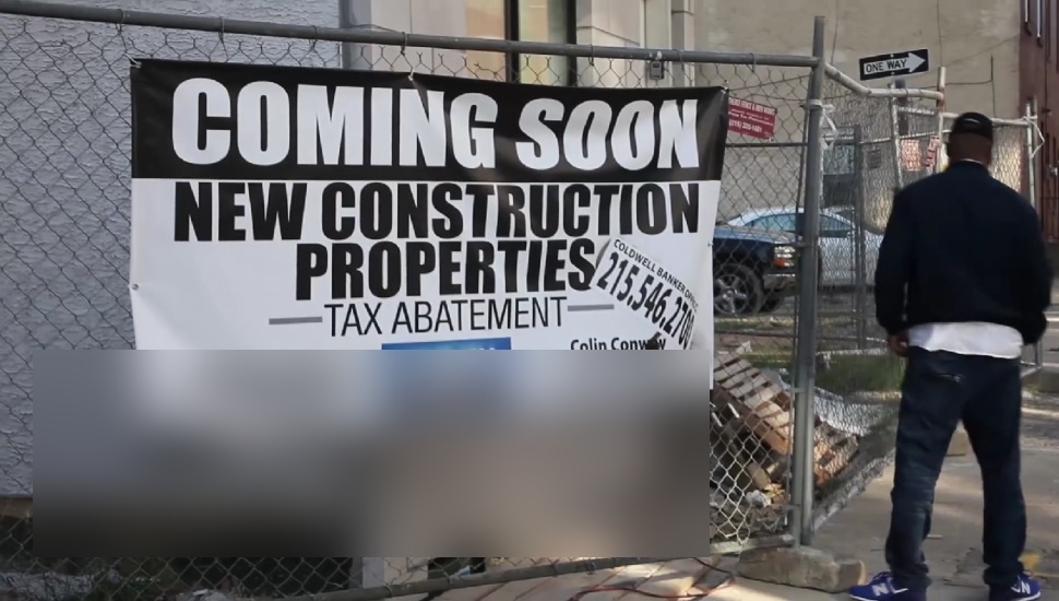 A man stands in front of a "Coming Soon: New Construction Properties" sign on a chain-link fence in Philadelphia's Francisville neighborhood.