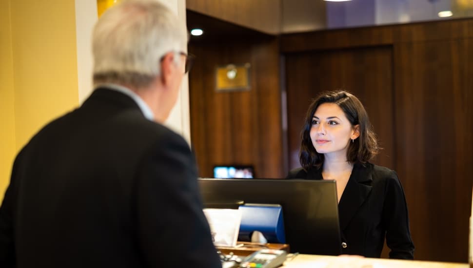 Young woman helps a businessman at a hotel reception desk, both smiling in a modern, elegant lobby.